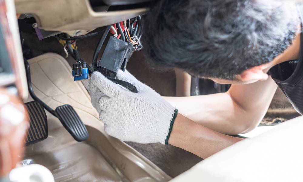 An automotive technician fixing the electrical system of a car as he wears insulated gloves and removes the connector.