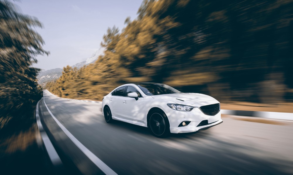 A four-door white sedan zooming down an open road in the day as all components in the car function properly.