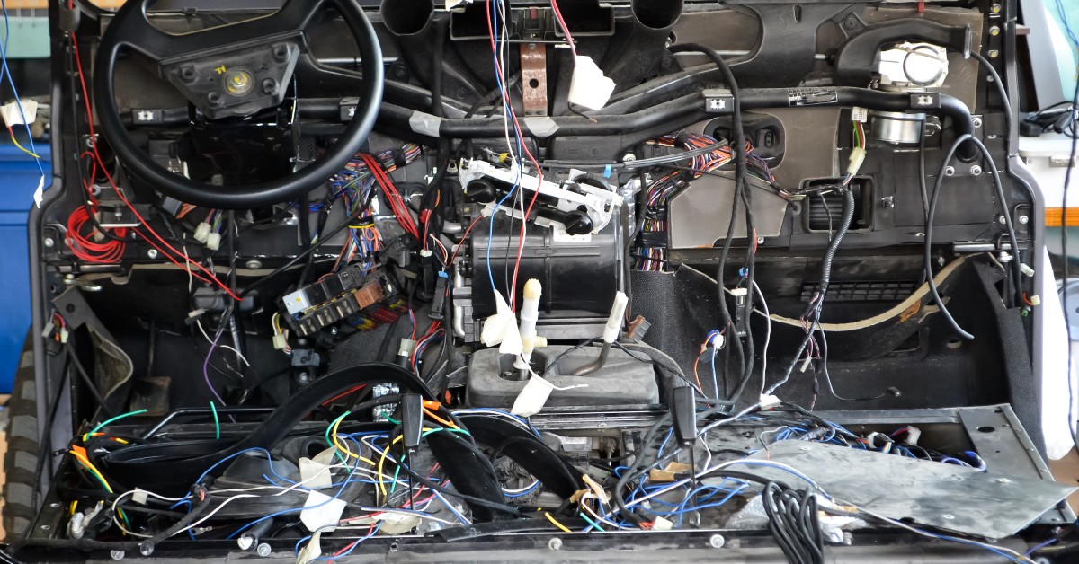 The interior cabin of a car has all the electrical areas open, exposing the wires and automotive electric connectors.