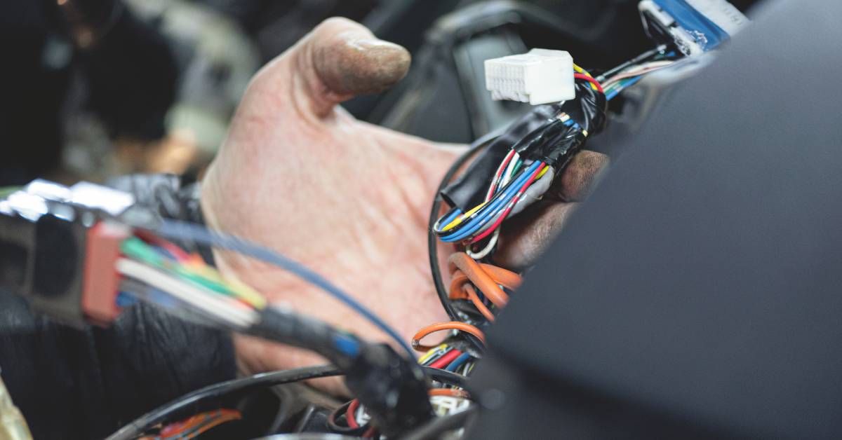 A hand holds the various strands of electric wires connected to a vehicle and two electrical connectors.