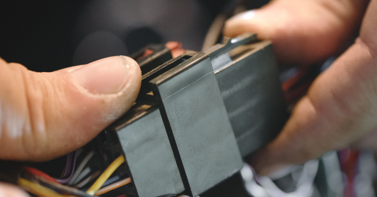 A pair of hands connects two pieces together to set up a car's sound system. The hands are pushing the two connectors together.