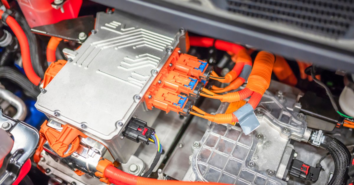 The interior of an electric vehicle engine. Many bright orange connectors and cables are coming from the silver center block.