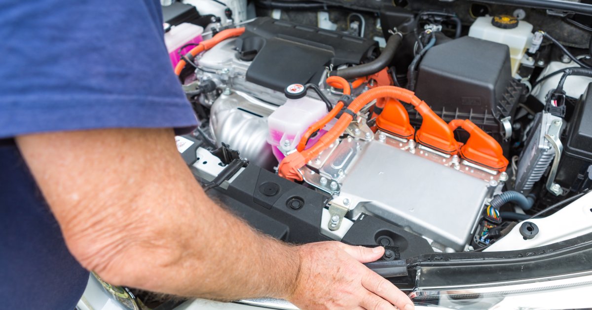 A technician standing over the open hood of a hybrid vehicle. You can see many wires and connectors hooked up to the engine block.