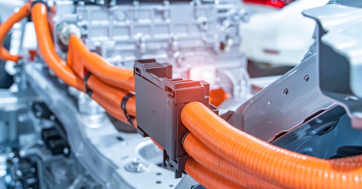 Several thick orange cables are coming out of both sides of a large silver connector block in an electrical system.