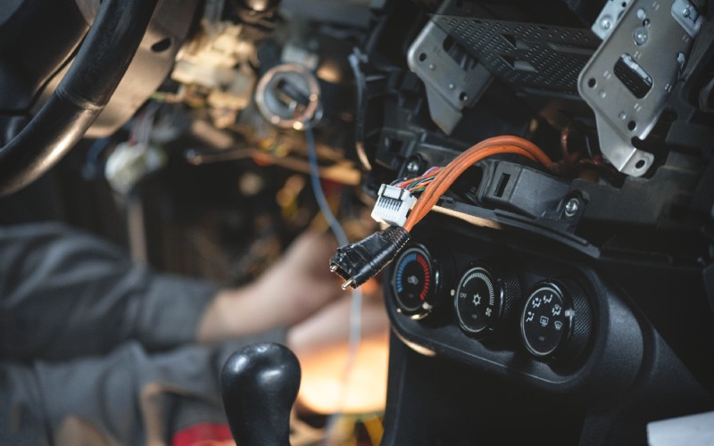 A pair of wires is coming out of an open cavity in a vehicle's dash. These connectors and cables hook up to the car's alarm.