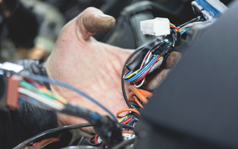 An engineer puts together a car's electrical system. He clutches a bundle of wires, and a white connector is at the top.