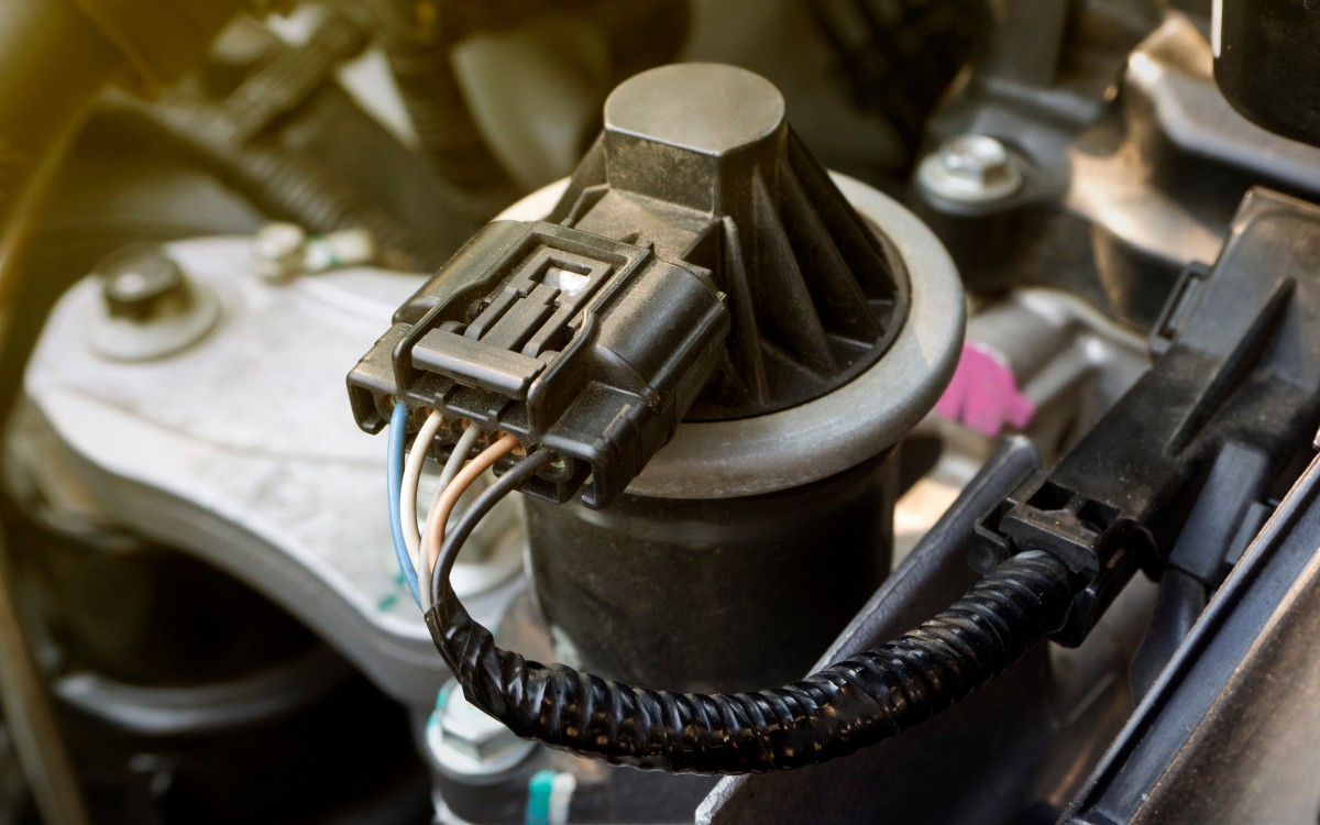 Close up of a vehicle engine's EGR valve. Several wires are coming out of an electrical connector that holds them together.