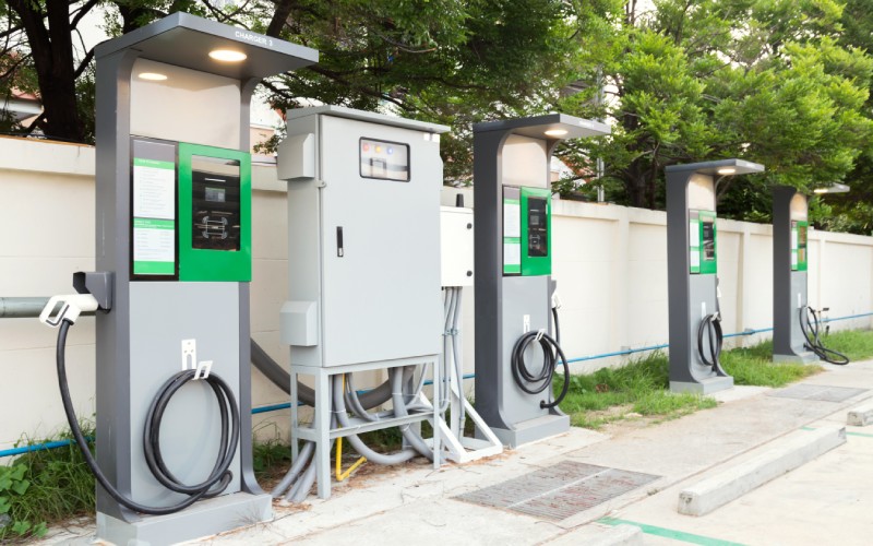 A row of electric vehicle charging stations connected to a large breaker. The cables are neatly wound up.