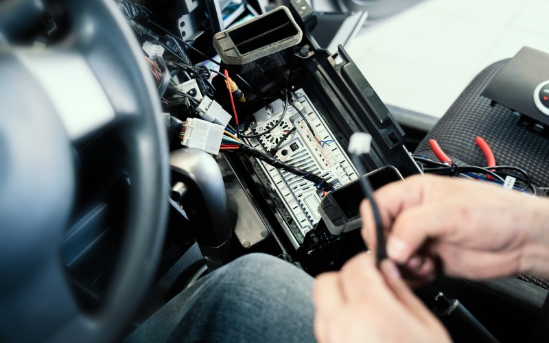 Close-up of hands working on a car's internal console, holding a black wire leading to the center unit.