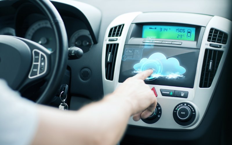 A man in a car is using the touchscreen on his infotainment system. The screen features an image of a cloud.