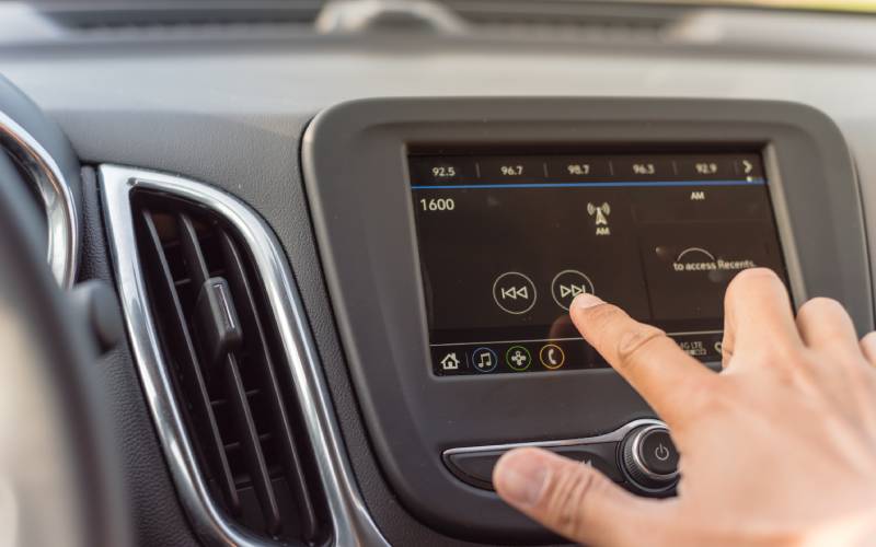 Closeup of a hand using a car's center console infotainment system. A finger is using the touchscreen to touch an arrow button.