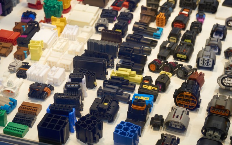 Many automotive connectors in various shapes, sizes, styles, and colors laid out in a grid formation on a flat surface.