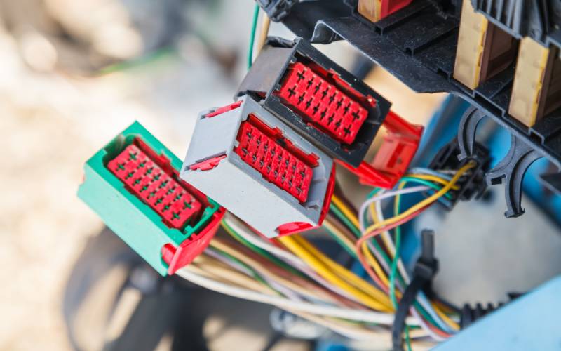 Three red connectors in different colored shells. Several wires are coming out the back of it and into an electrical system.