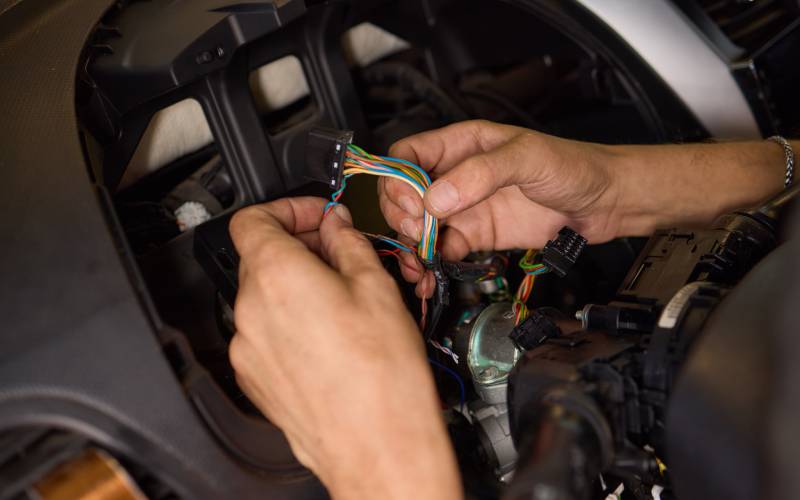 Closeup of a pair of hands working on the inside of a car's steering wheel. They're spreading apart some colorful wires.