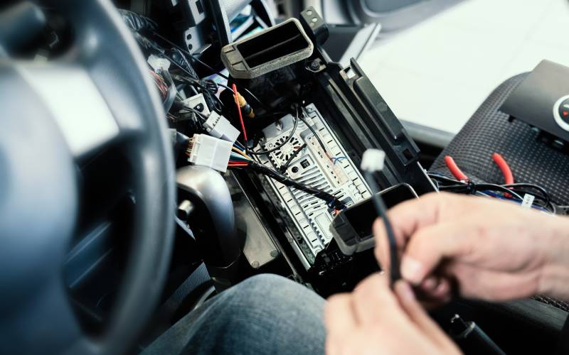 A pair of hands working with a thin black wire. The cables lead to a connector hanging from the open center console of a vehicle.