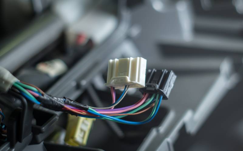 A pair of white and black automotive connectors with several colorful wires coming out of them are being taped together.