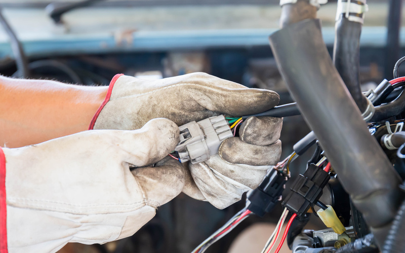 A person wearing white gloves holds a light gray colored automotive connector while performing car maintenance.