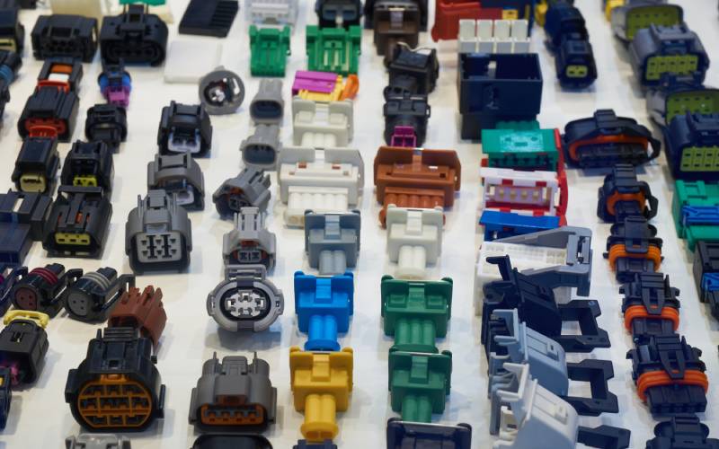 Many different cable connectors lined up on a plain, white surface. They are different colors and shapes.