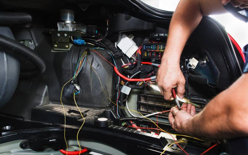 A close-up of someone using a tool to work with multi-colored wires inside a car’s electrical system.