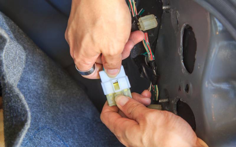A pair of hands wearing a ring on one pointer finger connects wires using a plastic connector in a car.
