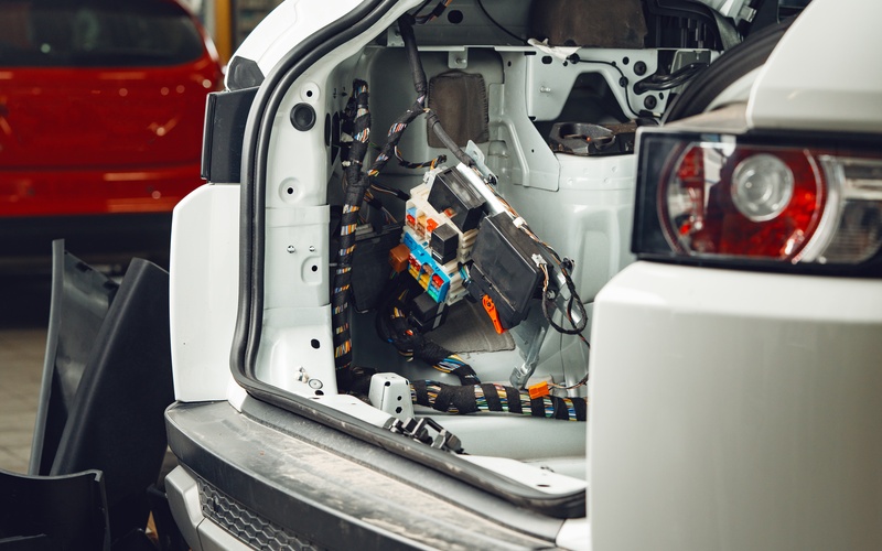 An exposed electrical system of a white car. The system has many connectors and colorful wires.