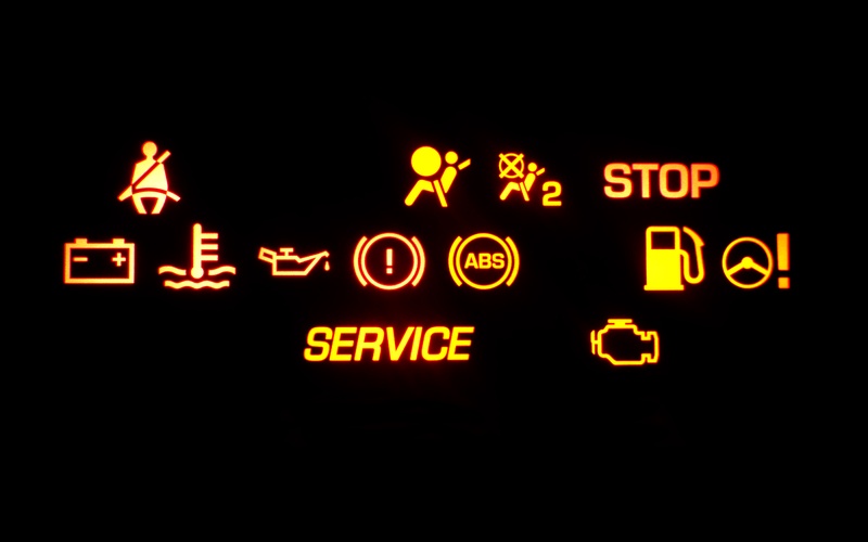 A car dashboard with many different orange warning lights lit up, including a seatbelt light and a gas light.