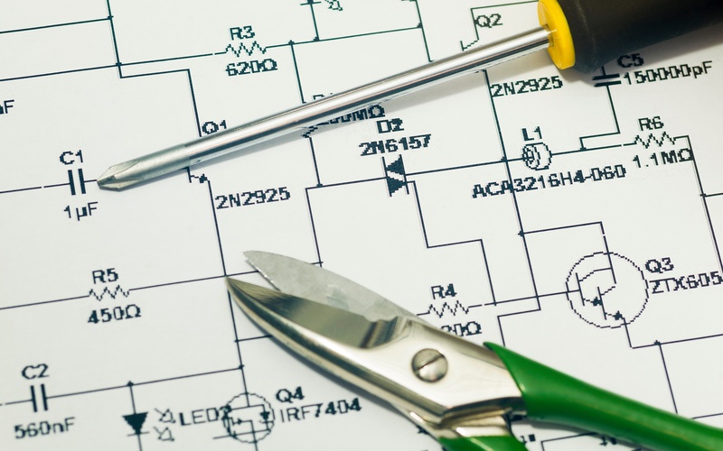 A screwdriver with a black and yellow handle and pair of wire cutters with green handles resting on an electrical diagram.