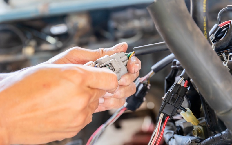 A close-up of a person's hands with dirt under their finger nails as they hold a light gray wire connector in a car.