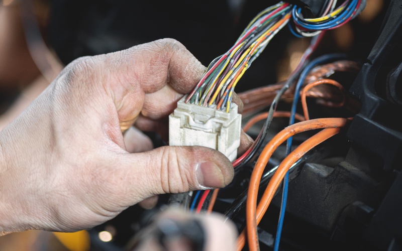 A hand covered in dirt holding a white wire connector with thin, colorful wires extending from it.