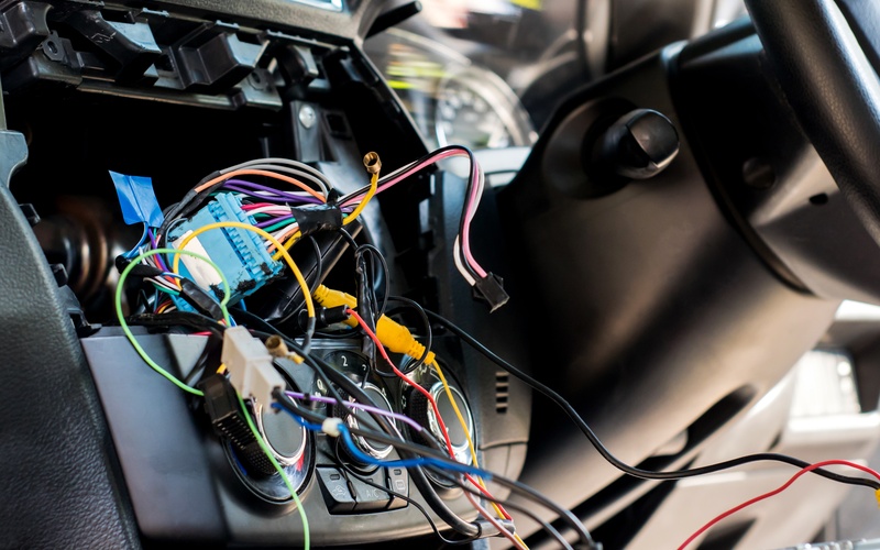 A close-up a vehicle's exposed electrical system. Colorful wires hang down next to the steering wheel.