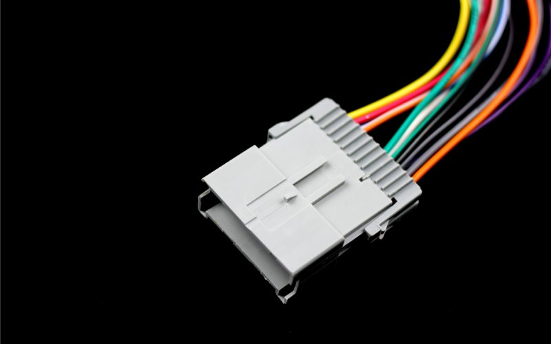 A gray automotive connector with many thin, colorful wires extending from it on a black background.