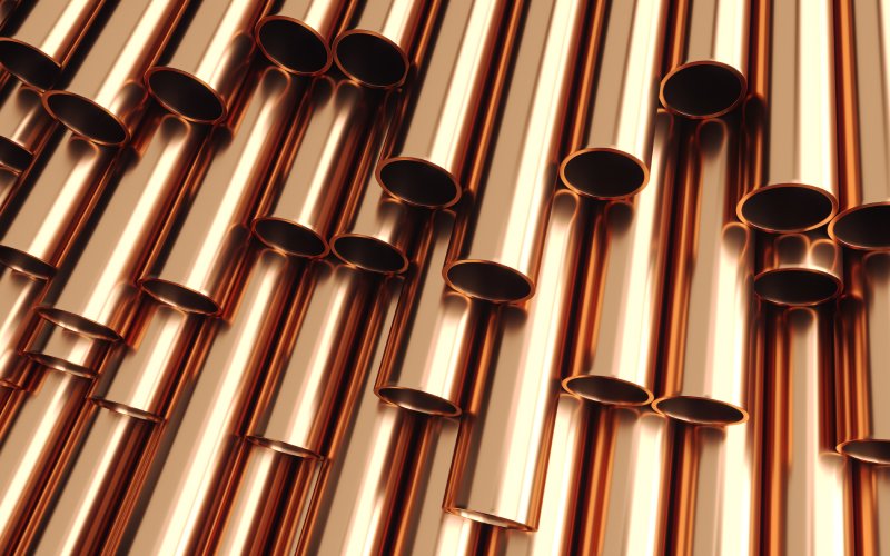 A pile of shiny, copper alloy tubes stacked on top of each other. The tubes are reflecting light.