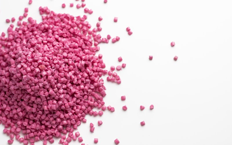 A small, neat pile of pink granules of polyamide with some granules spilling out on a white background.