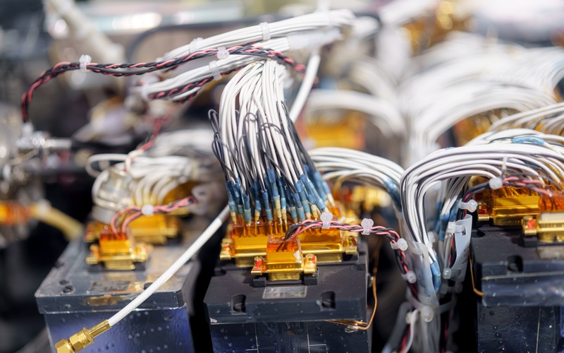 A close-up of electrical connectors being manufactured. The exposed wires are white, red, and black.