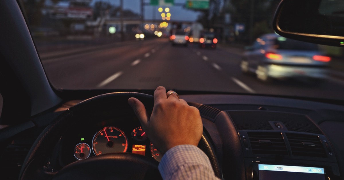 A driver takes his car for a ride on the highway during the nighttime. The car dashboard glows in the dark cabin.