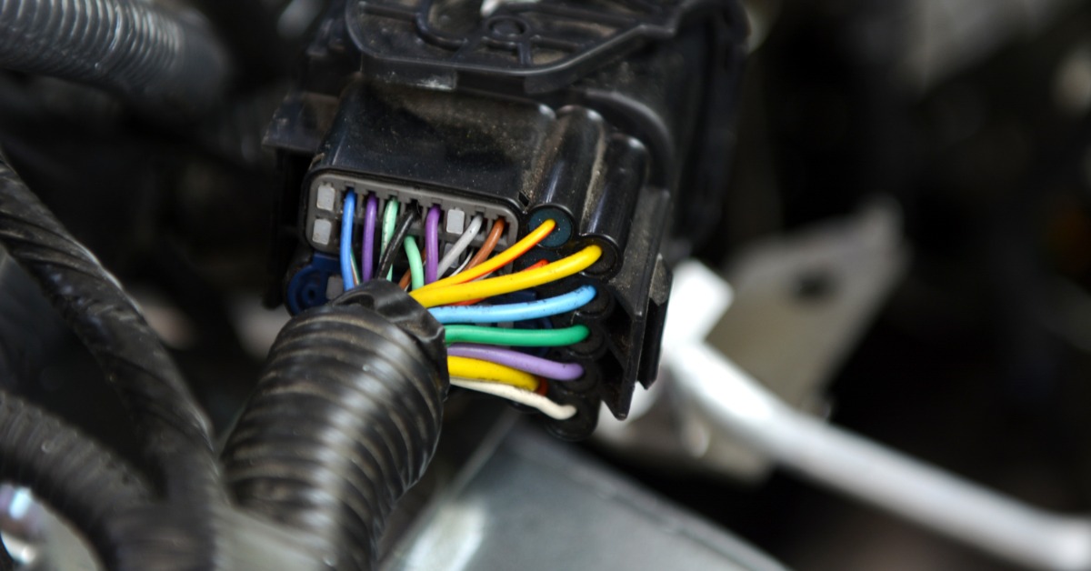 A black automotive connector next to black tubes in a vehicle. The connector has many colorful wires running out of it.