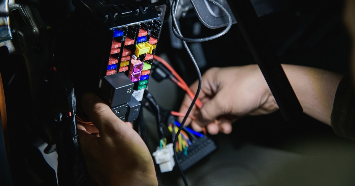 A person disassembling a large black block on their car dashboard to reveal many colorful fuses, connectors, and wires.