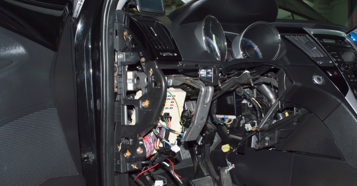A parked car with its dashboard dismantled to expose many automotive connectors and electrical cables underneath.