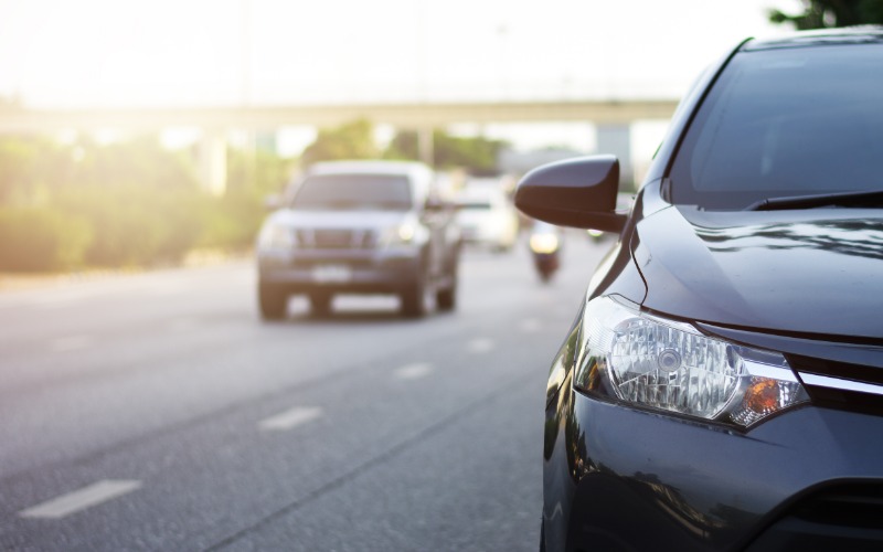 A clean, black car driving down the highway during the daytime. Many cars and one motorcycle travel nearby.