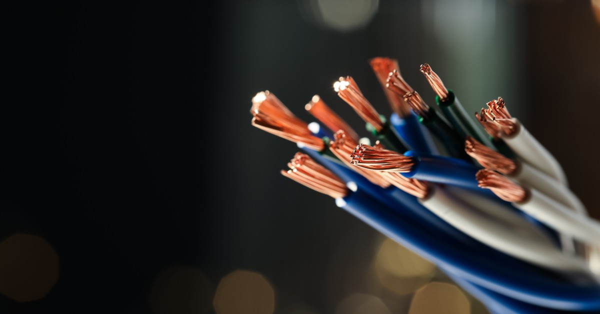 Colorful copper wires with their insulation partially stripped away. Bright lights are barely visible in the distance.