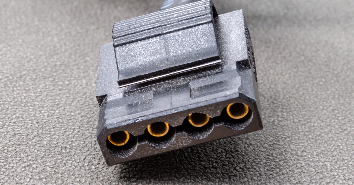 A black four-pin connector sitting on a black, bumpy surface. The connector has a wide, bulky black cable.