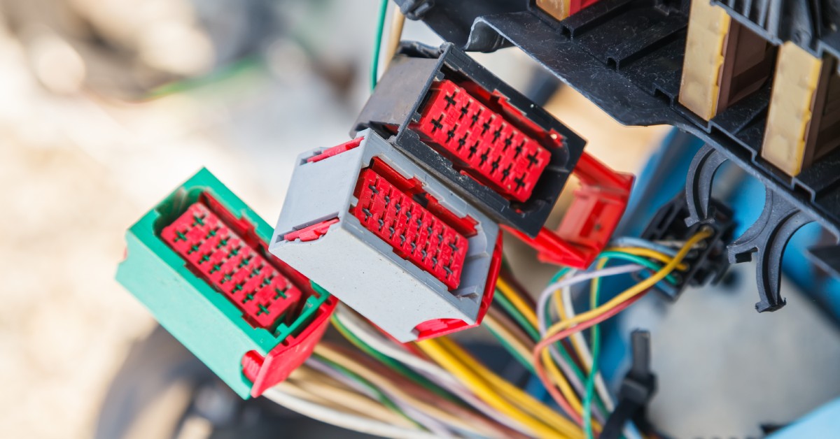 Three electrical connectors with many colorful wires attached to them. Sunlight is shining behind the connectors.