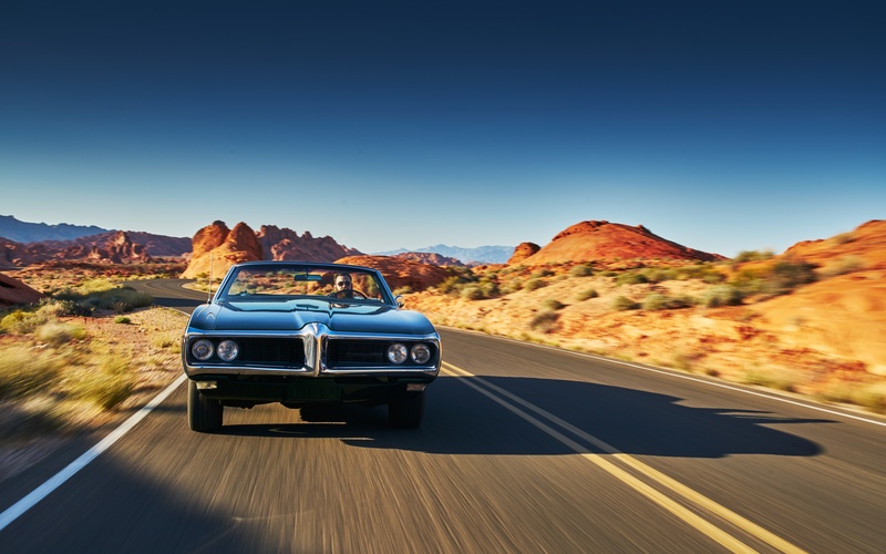 A person driving a car with the top down on a sunny day. They are driving on a road leading through the desert.