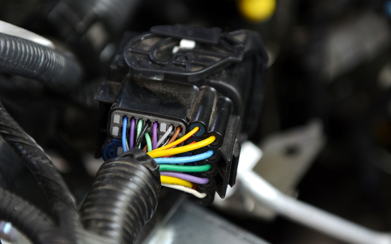 A connector inside a car. The wires attached to the connector are blue, purple, green, brown, gray, and yellow.
