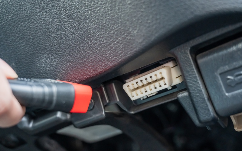 A person plugging a cable into an automotive connector inside their vehicle. The cable has a red tip.