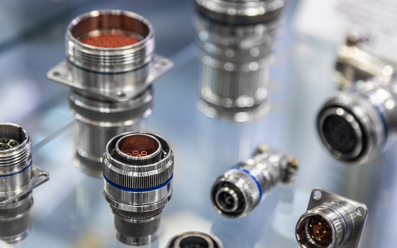 Nine metal electrical connectors inside a glass case. The connectors are in different sizes and positions.