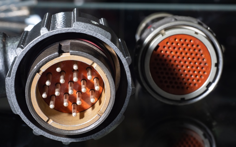 Two automotive connectors on a glass surface. The male connector has sixteen pins arranged inside a black housing.