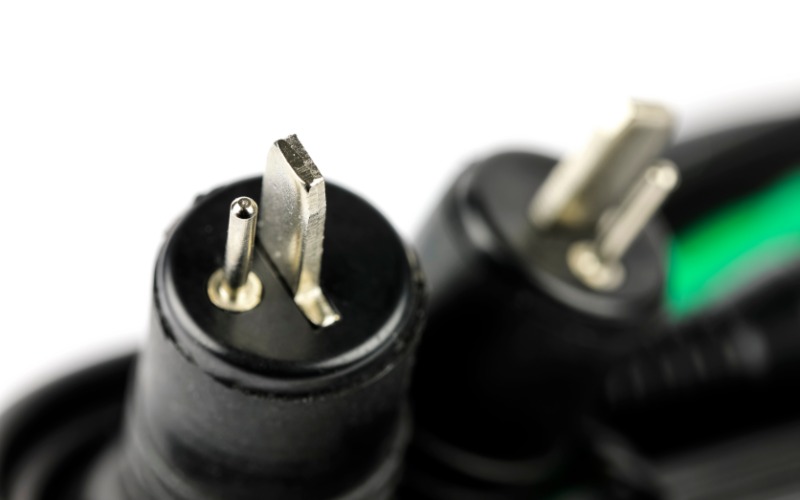 Two black two-pin automotive connectors with metal ends. The connectors sit in front of a white wall.