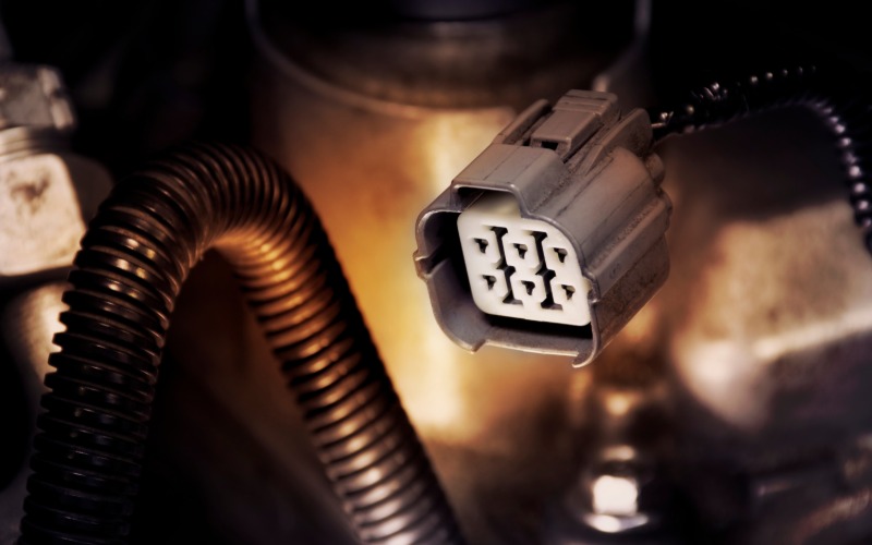 A white six-pin automotive connector inside a dark gray housing. The connector is attached to a black cord.