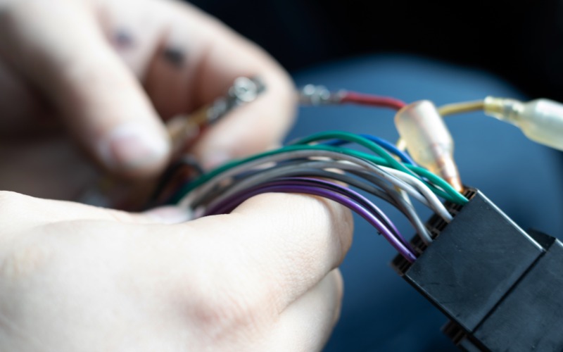 A mechanic using their bare hands to repair colorful wire connectors attached to an automotive wiring harness.